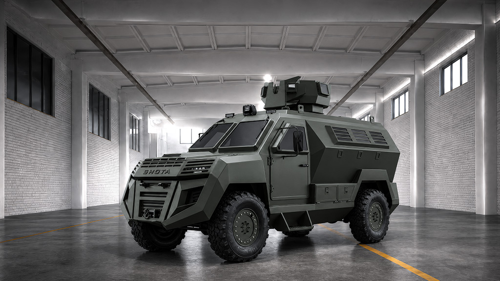 A military armored vehicle, specifically Shota MRAP from Timak, situated in a large, dimly lit warehouse or hangar with white brick walls and a concrete floor.