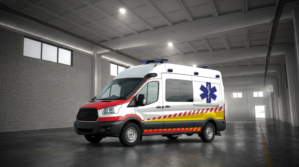 A white ambulance with red and yellow stripes parked in a large, dimly lit warehouse or garage.