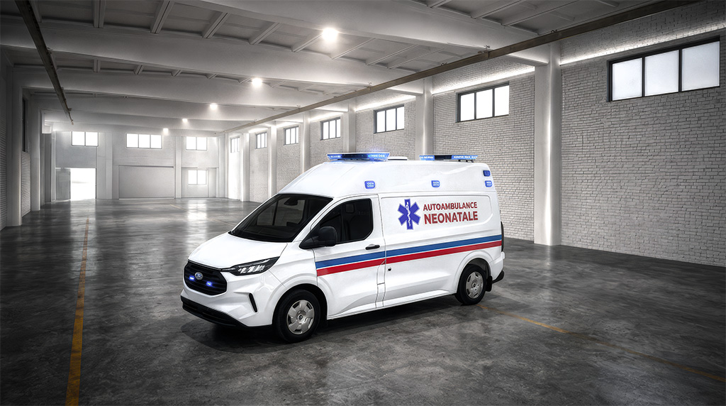 A white ambulance with blue and red stripes parked in a large, empty warehouse with white walls and a concrete floor.
