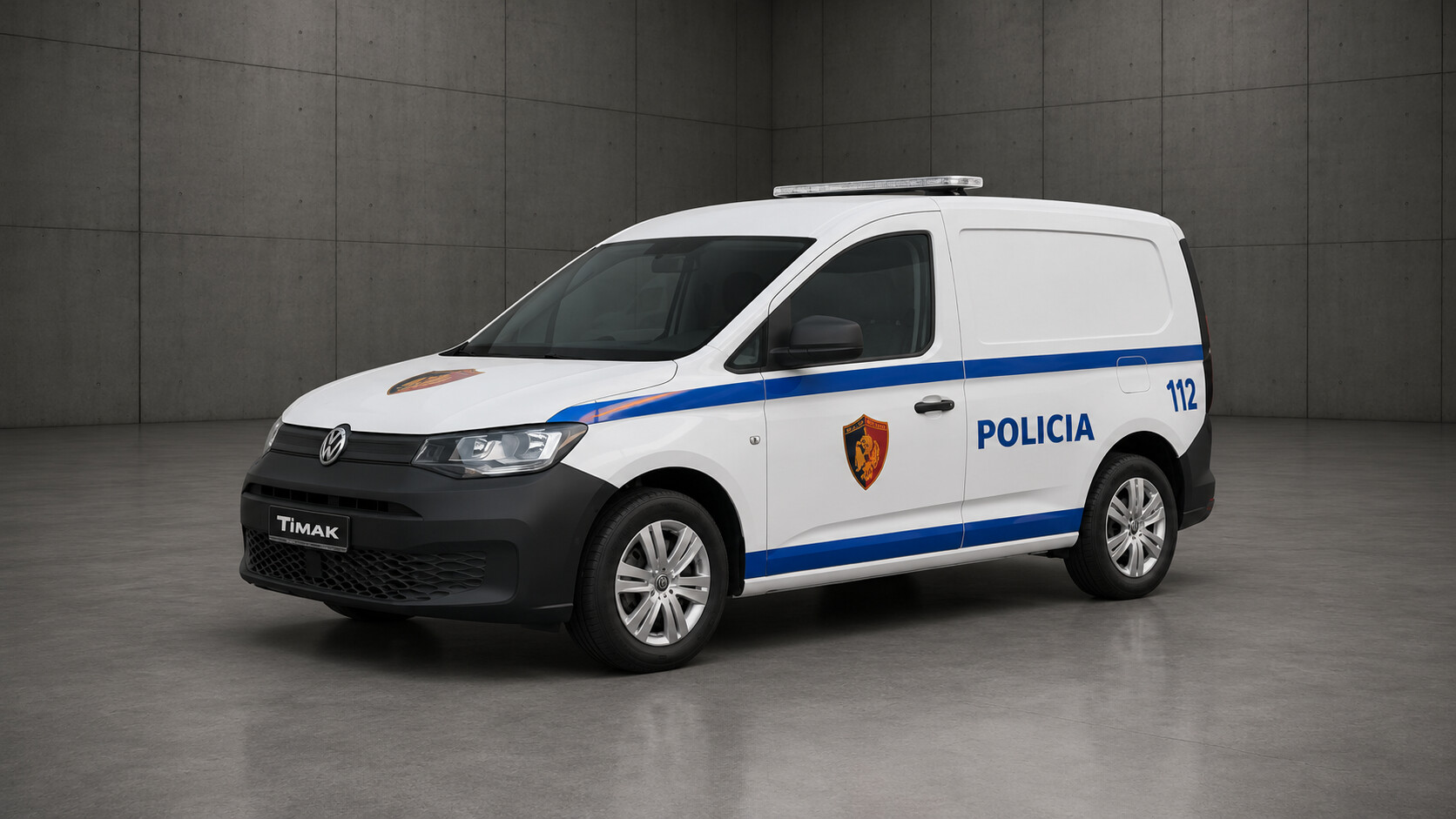 A white Volkswagen Transporter van with blue stripes and police markings, set against a gray concrete wall and floor.