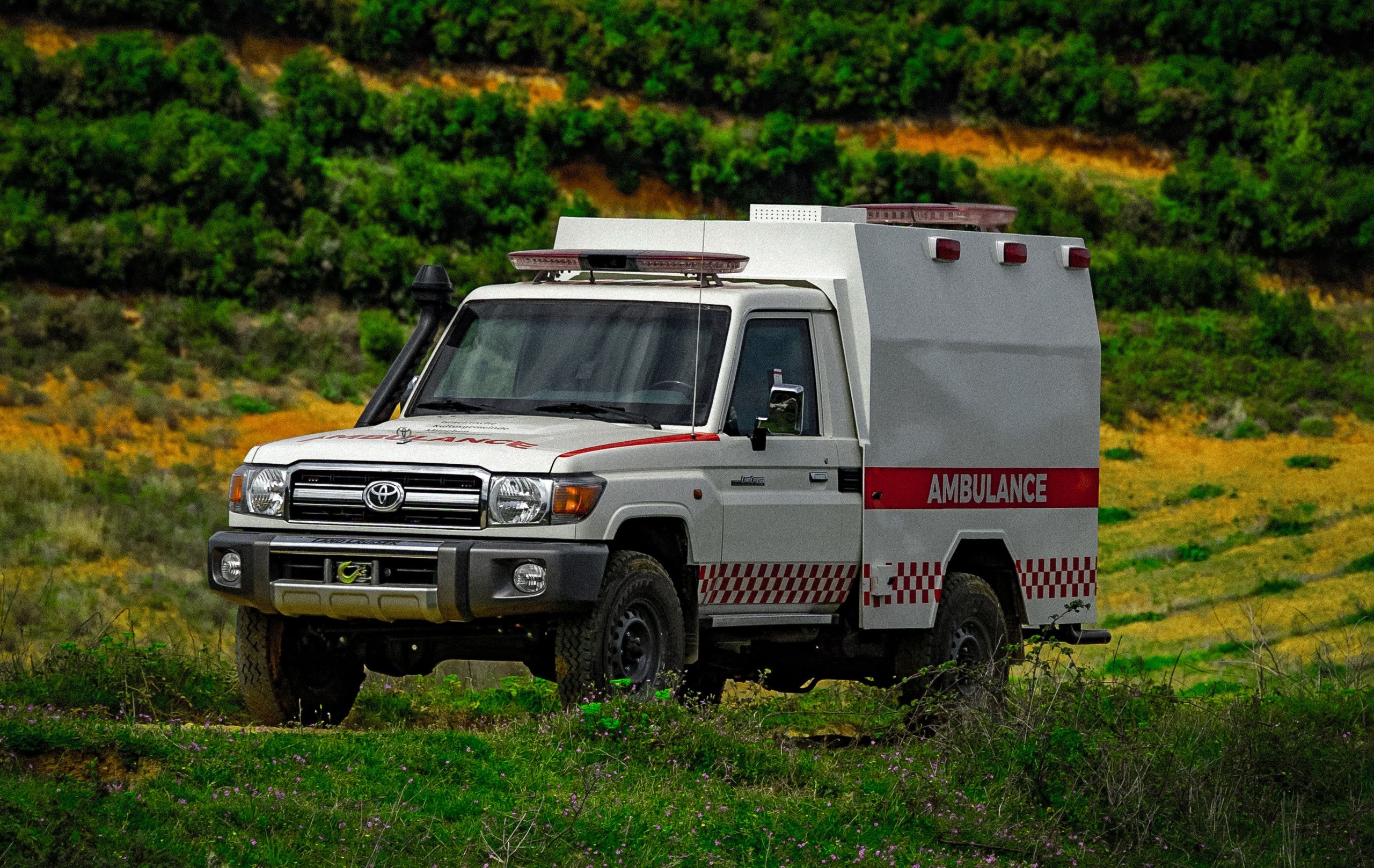 A white ambulance with red detailing is parked in a grassy field.